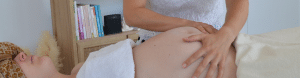 Femme enceinte recevant un massage prénatal du dos au 9ème mois de grossesse en position sur le côté.